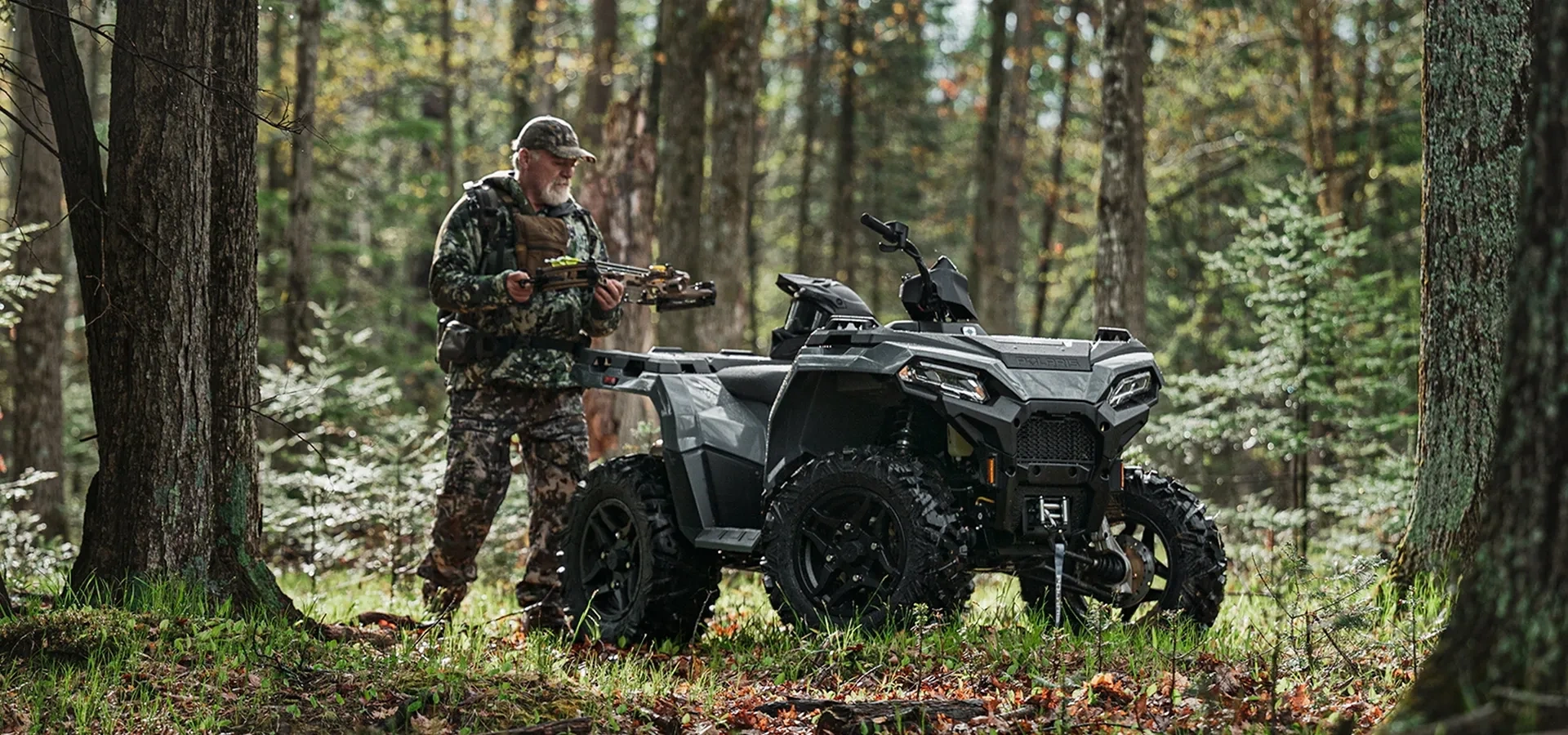Chasseur à côté d’un VTT Polaris Sportsman 500 2027 stationné en forêt.