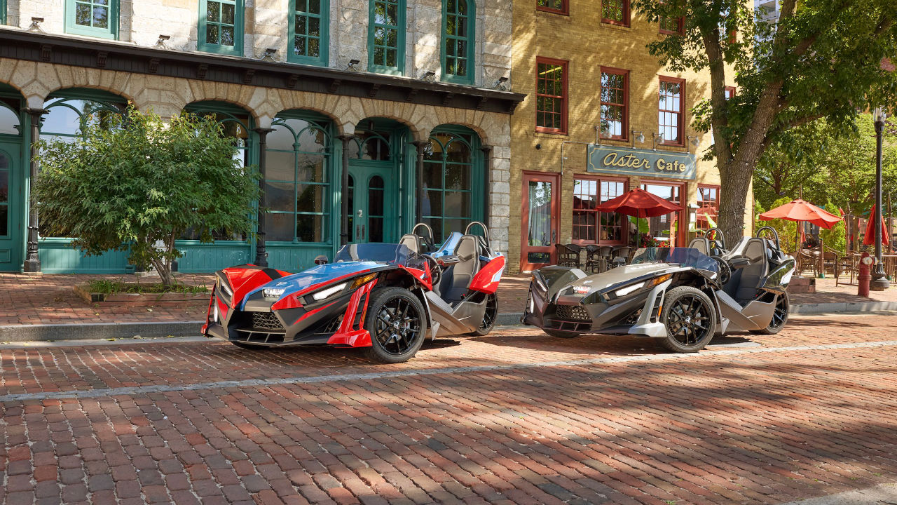 deux véhicules Polaris Slingshot devant un café, en ville