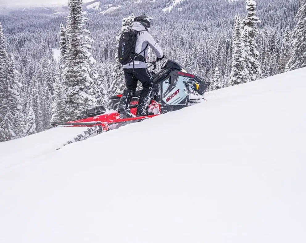 Motoneige Polaris Pro RMK 2026 noire et rouge traversant un sentier enneigé en pleine vitesse, vue latérale gauche.