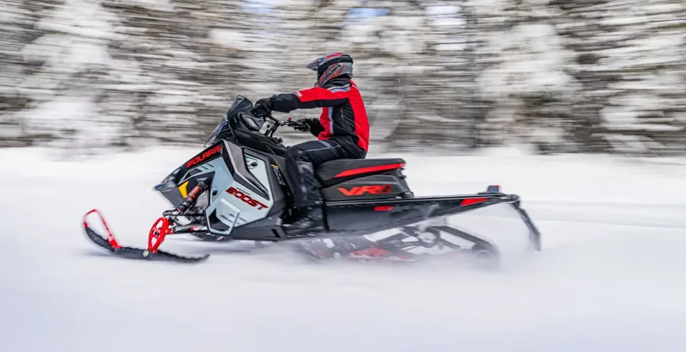 Motoneige Polaris Indy VR1 2026 bleue et noire roulant sur un sentier enneigé bordé d’arbres.