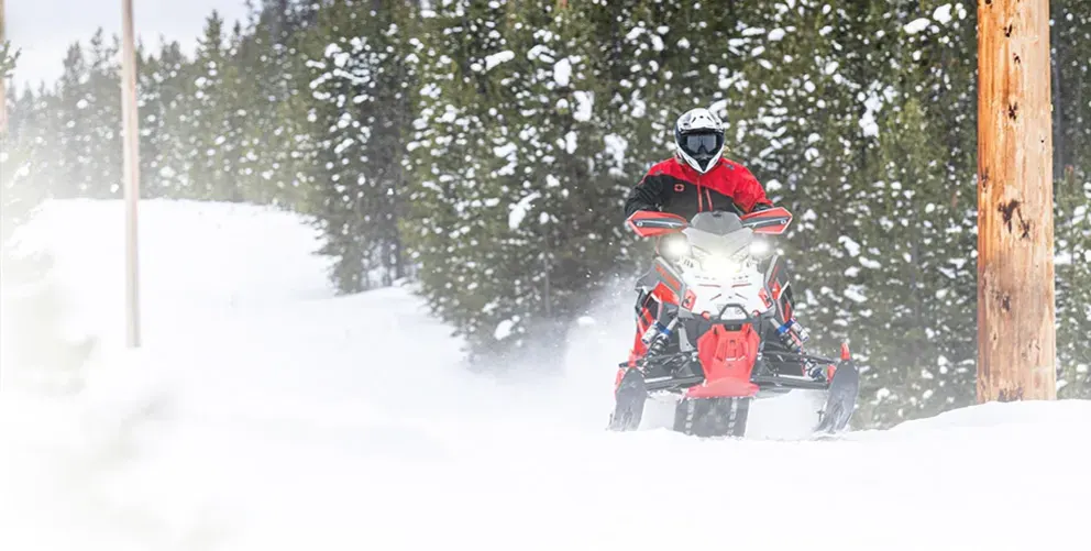 Motoneige Polaris Indy XCR 2026 bleue avec skis noirs traversant la neige à haute vitesse, vue de face trois quarts.