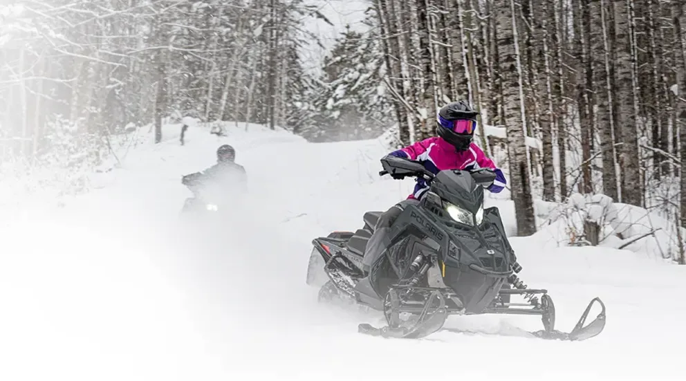 Motoneige Polaris Indy XC 2026 grise et rouge en virage rapide sur sentier enneigé, forêt en arrière-plan.