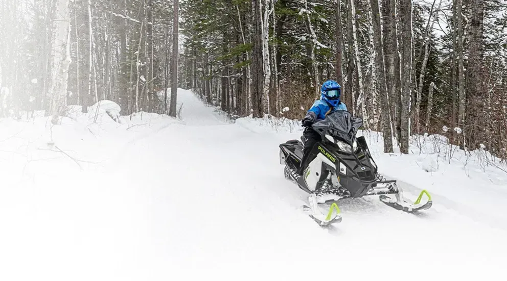 Motoneige Polaris Indy SP 2026 noire et blanche roulant en solo sur un sentier forestier enneigé.
