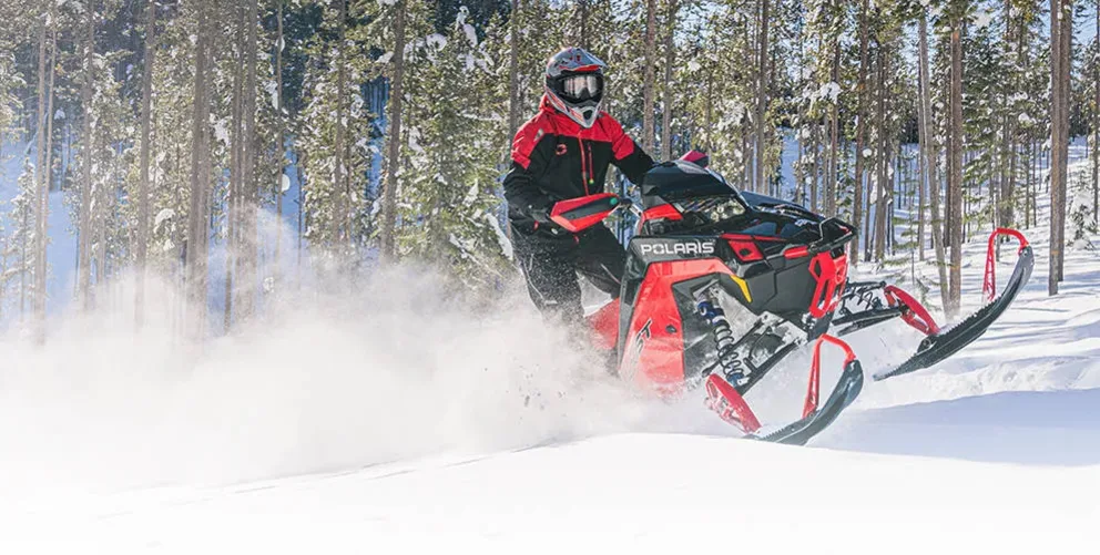Motoneige Polaris Switchback Assault 2026 rouge et noire attaquant un sentier enneigé à vive allure.