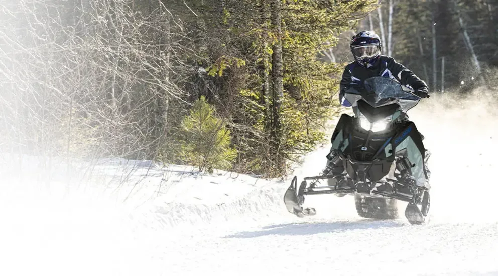 Motoneige Polaris Switchback XC 2026 noire et grise roulant en terrain mixte, entre forêt et poudreuse.