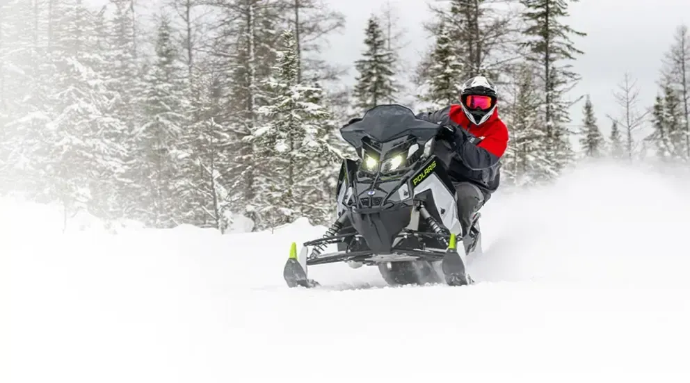 Motoneige Polaris Switchback SP 2026 noire et rouge glissant sur un large sentier enneigé, forêt à l’arrière-plan.