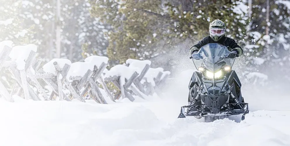 Motoneige Polaris Voyageur XC 155 2026 noire équipée d’accessoires de travail roulant dans la neige profonde.