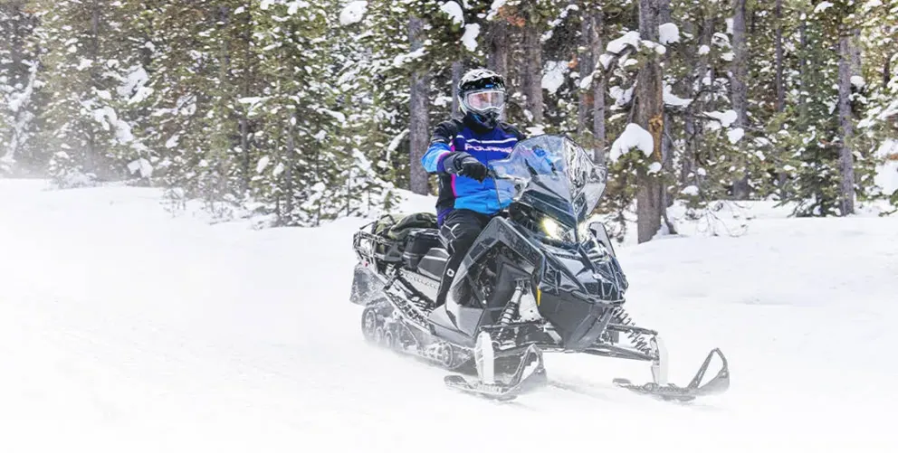 Motoneige Polaris Voyageur SP 155 2026 blanche et rouge avançant dans une forêt enneigée en hiver.