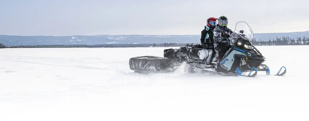 Motoneige Polaris Titan 2026 noire et rouge tractant une charge sur un sentier enneigé de montagne.