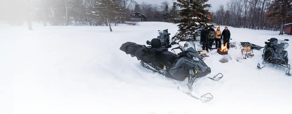 Two Polaris snowmobiles parked on the snow in nature.